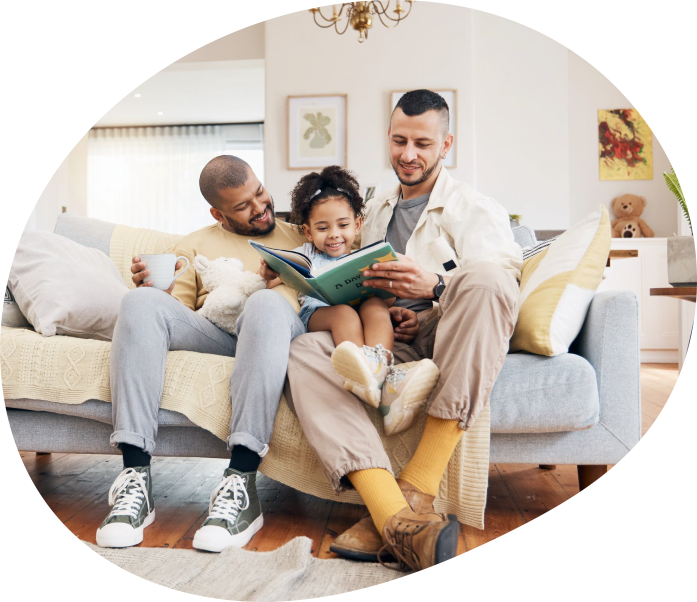 Gay couple and their daughter sitting on a couch reading a book